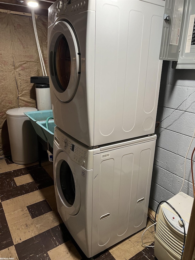 laundry room with laundry area, stacked washing maching and dryer, concrete block wall, and electric panel