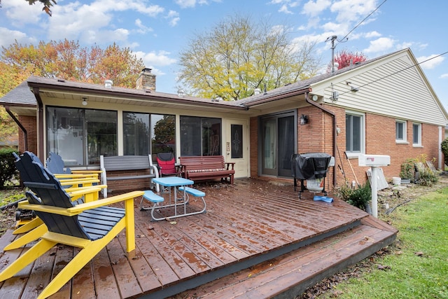 rear view of house with a sunroom, a wooden deck, a chimney, and brick siding