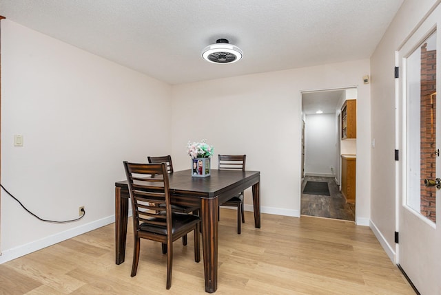 dining room featuring light wood-style flooring, baseboards, and a textured ceiling