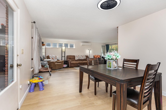 dining space with a textured ceiling, light wood finished floors, a wall unit AC, and baseboards