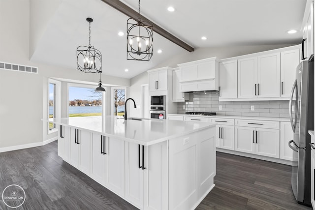 kitchen featuring dark wood-style floors, a center island with sink, stainless steel appliances, lofted ceiling with beams, and decorative backsplash