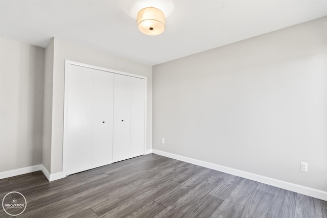 unfurnished bedroom with a closet, dark wood-style flooring, and baseboards