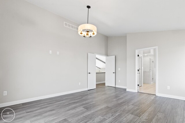 interior space with lofted ceiling, wood finished floors, visible vents, baseboards, and an inviting chandelier