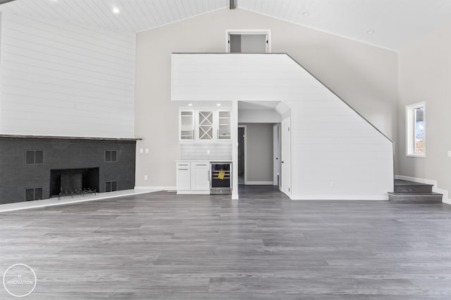 unfurnished living room featuring baseboards, visible vents, wood finished floors, a fireplace, and high vaulted ceiling