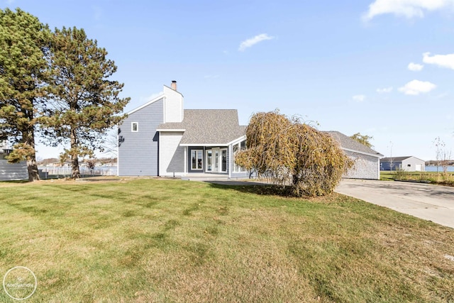 view of front facade featuring concrete driveway, french doors, roof with shingles, a chimney, and a front yard