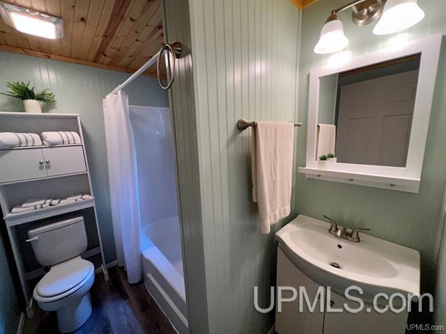 bathroom featuring toilet, wood ceiling, wood finished floors, shower / bathtub combination with curtain, and vanity