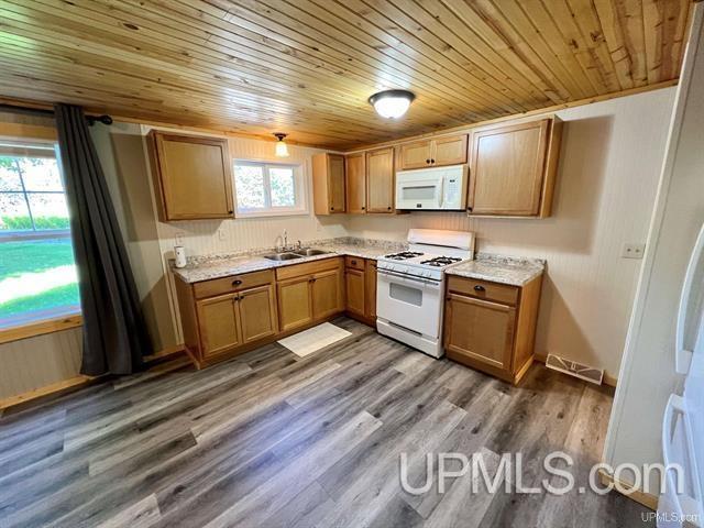 kitchen with white appliances, dark wood-style floors, brown cabinets, and a sink