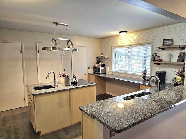 kitchen with a kitchen island with sink, stainless steel microwave, a sink, and backsplash