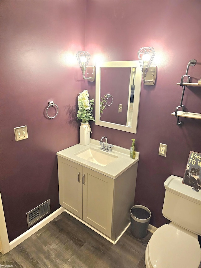 half bathroom featuring visible vents, toilet, vanity, wood finished floors, and baseboards