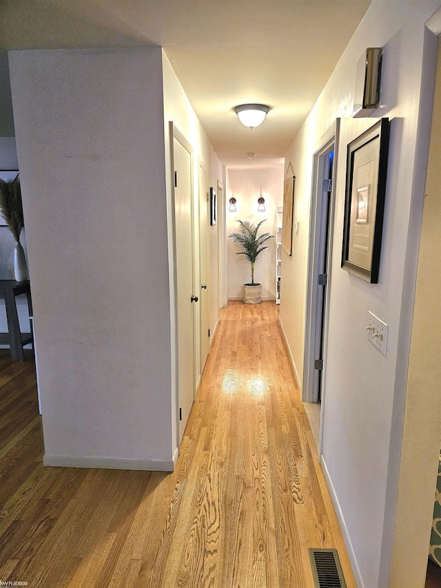 hallway with light wood finished floors, visible vents, and baseboards