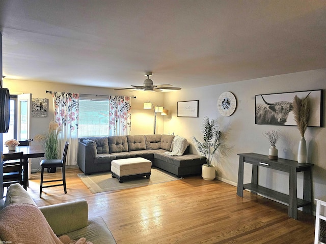 living area with light wood-style floors, baseboards, and a ceiling fan