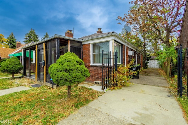 bungalow-style home with a sunroom, a chimney, fence, and brick siding