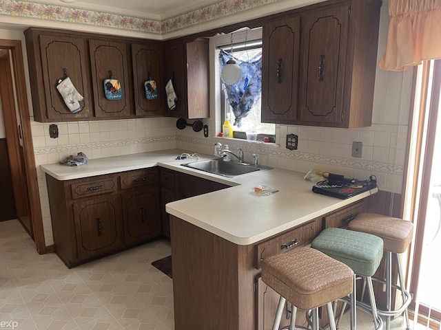 kitchen featuring a peninsula, a kitchen bar, a sink, and light countertops