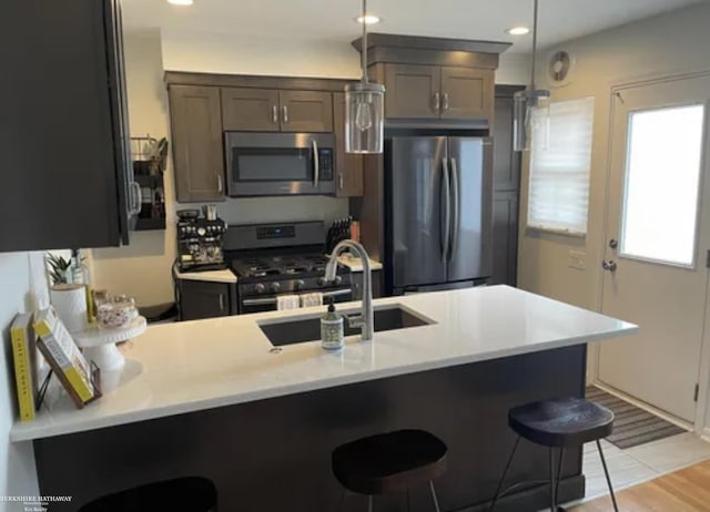 kitchen with appliances with stainless steel finishes, a peninsula, light countertops, a kitchen bar, and a sink