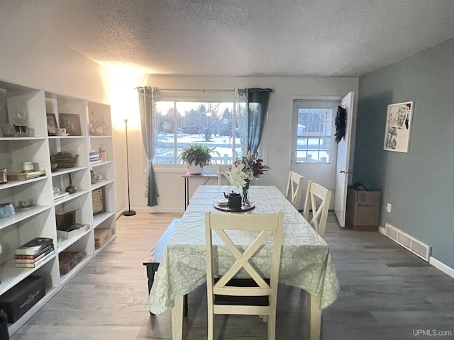 dining space featuring baseboards, a textured ceiling, visible vents, and wood finished floors