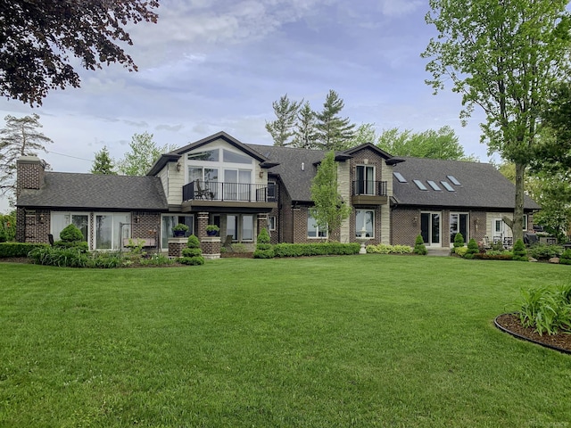 view of front of home with a balcony, a shingled roof, a front lawn, and brick siding