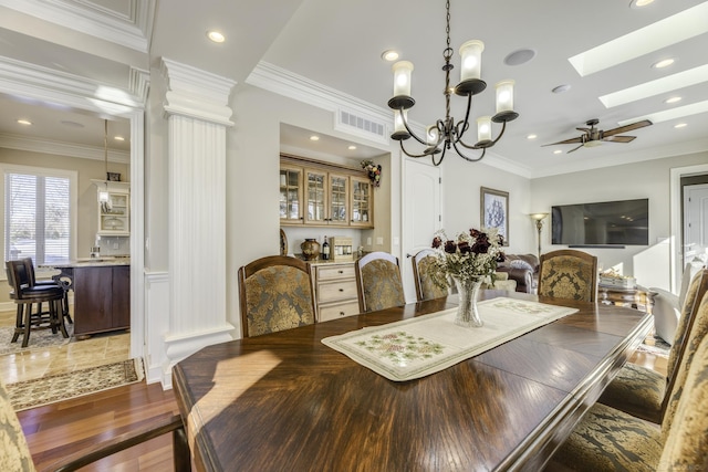 dining area with a skylight, visible vents, ornamental molding, light wood-type flooring, and ceiling fan with notable chandelier