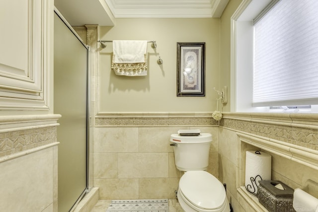 bathroom with a wainscoted wall, crown molding, tile walls, toilet, and a stall shower