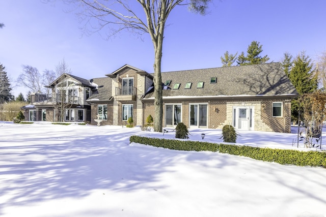 view of front of property featuring brick siding, a balcony, and roof with shingles