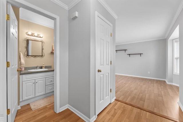 hall with ornamental molding, a sink, light wood-style flooring, and baseboards