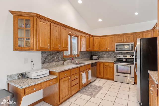 kitchen featuring backsplash, appliances with stainless steel finishes, brown cabinetry, vaulted ceiling, and a sink