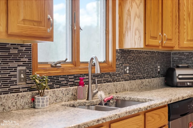 kitchen featuring decorative backsplash, a sink, light stone counters, and stainless steel dishwasher