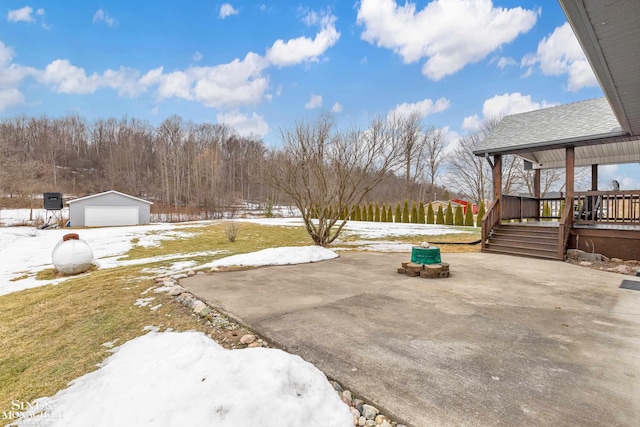 yard layered in snow featuring a patio area, an outdoor structure, a wooden deck, and a detached garage