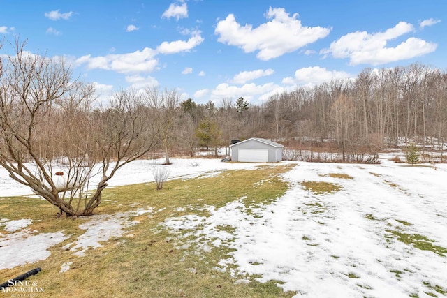 snowy yard featuring a garage, a forest view, and an outdoor structure