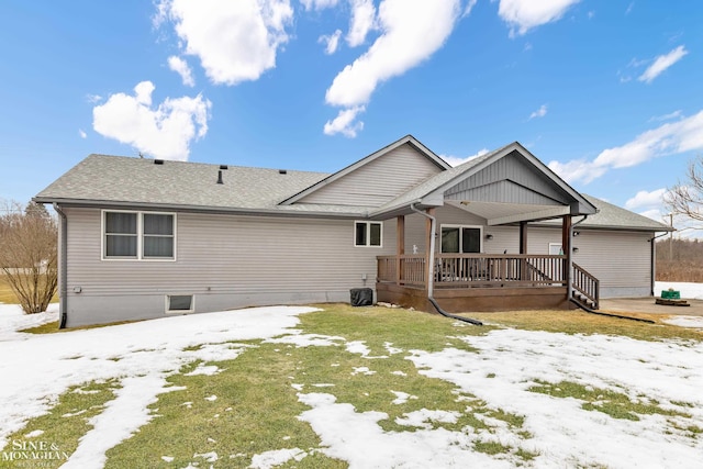 snow covered back of property with roof with shingles and a wooden deck