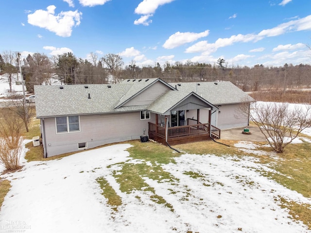 snow covered back of property featuring a shingled roof, cooling unit, and a wooden deck