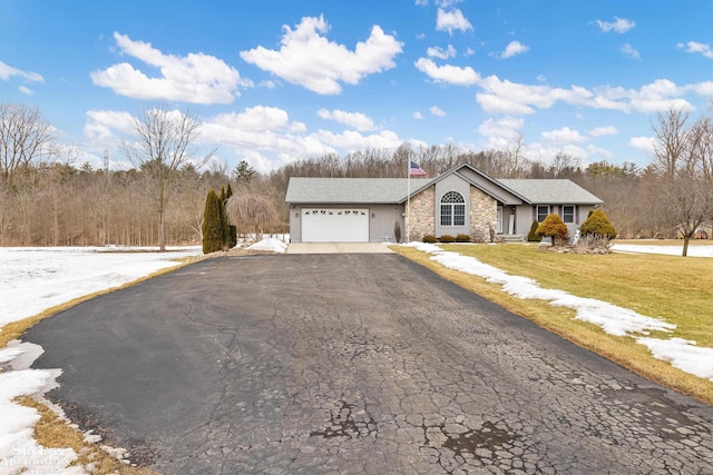 single story home featuring stone siding, a yard, an attached garage, and driveway