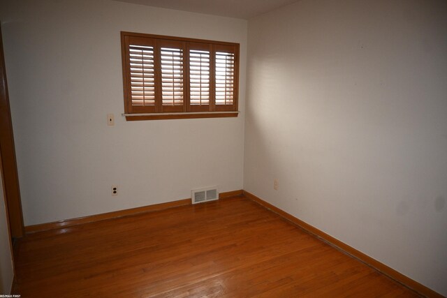 unfurnished room featuring wood finished floors, visible vents, and baseboards