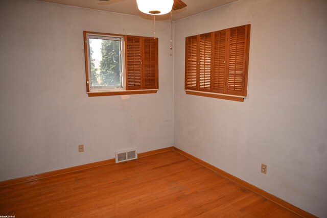 spare room featuring a ceiling fan, visible vents, baseboards, and wood finished floors