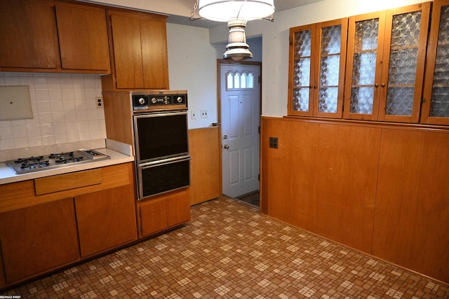 kitchen featuring brown cabinets, a warming drawer, light countertops, appliances with stainless steel finishes, and wood walls