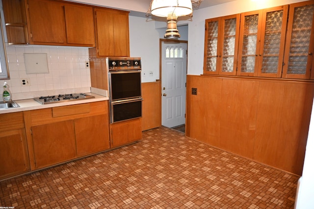 kitchen with a wainscoted wall, light countertops, stainless steel gas stovetop, brown cabinetry, and wood walls