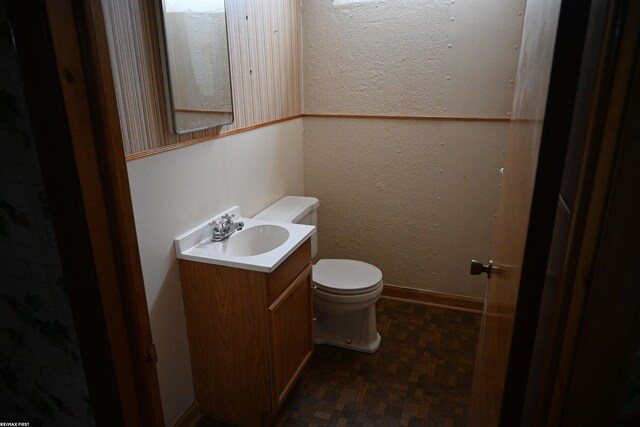 half bath featuring toilet, a textured wall, baseboards, and vanity