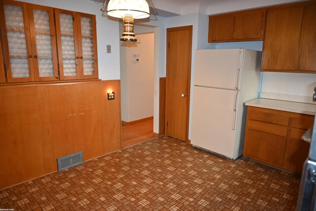 kitchen with visible vents, light countertops, freestanding refrigerator, brown cabinetry, and glass insert cabinets