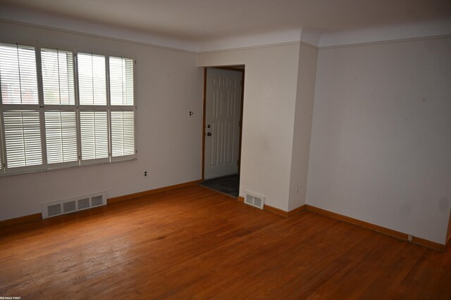 spare room with wood finished floors, visible vents, and baseboards