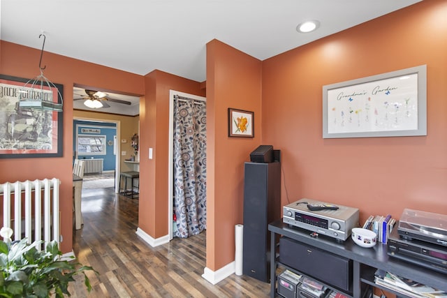 office area with baseboards, wood finished floors, a ceiling fan, and radiator