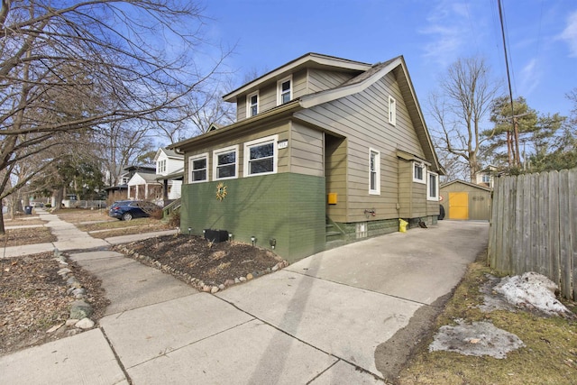 view of property exterior with driveway, brick siding, an outdoor structure, and fence