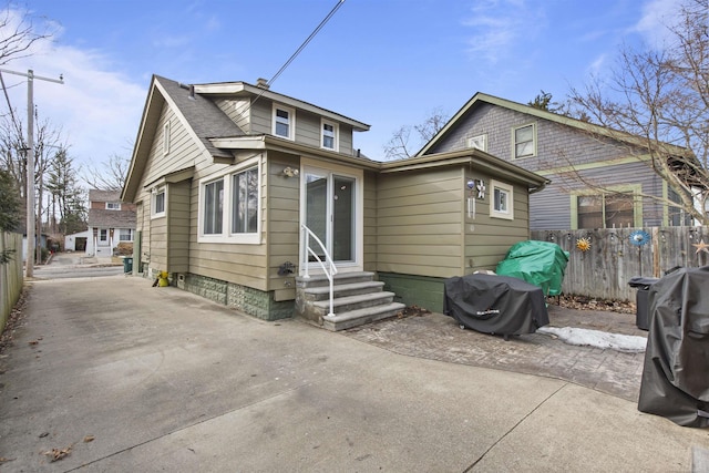 rear view of house featuring entry steps, a shingled roof, fence, and concrete driveway