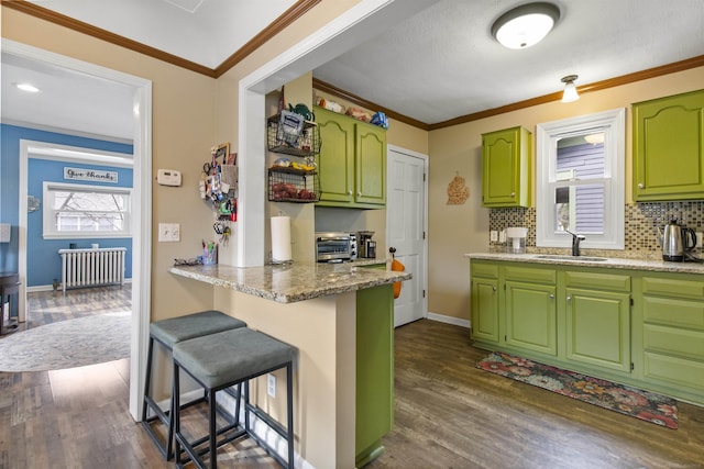 kitchen with dark wood-style flooring, radiator heating unit, ornamental molding, a sink, and a kitchen breakfast bar