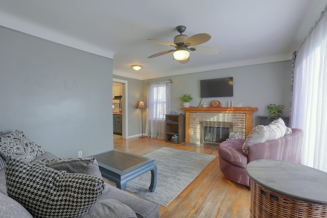 living room featuring light wood finished floors, a brick fireplace, a ceiling fan, and baseboards