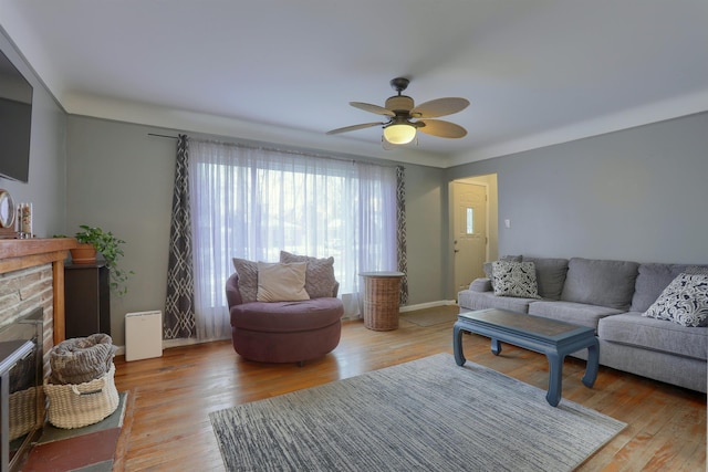 living area with a stone fireplace, light wood finished floors, and a ceiling fan