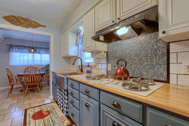 kitchen featuring tasteful backsplash, wood counters, cream cabinetry, under cabinet range hood, and a sink