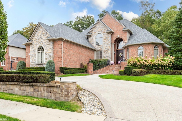 view of front of home featuring concrete driveway, stone siding, brick siding, and a shingled roof