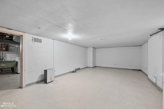 finished basement with concrete block wall, washer / clothes dryer, visible vents, and light floors