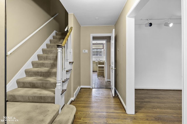 foyer entrance with stairs, wood finished floors, rail lighting, and baseboards