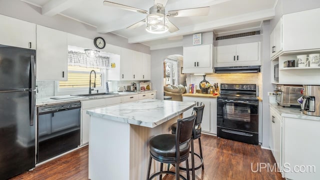 kitchen with arched walkways, under cabinet range hood, a sink, beam ceiling, and black appliances