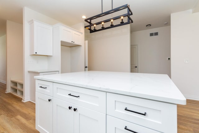 kitchen featuring light stone countertops, visible vents, white cabinets, light wood-type flooring, and a center island